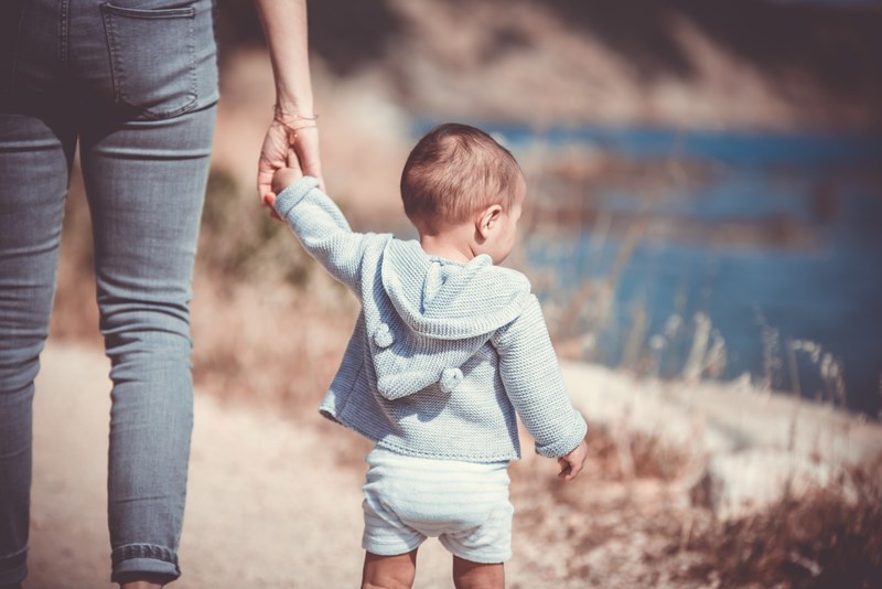 a parent holding her childs hand and walking by the water in a field, parent and child 4k