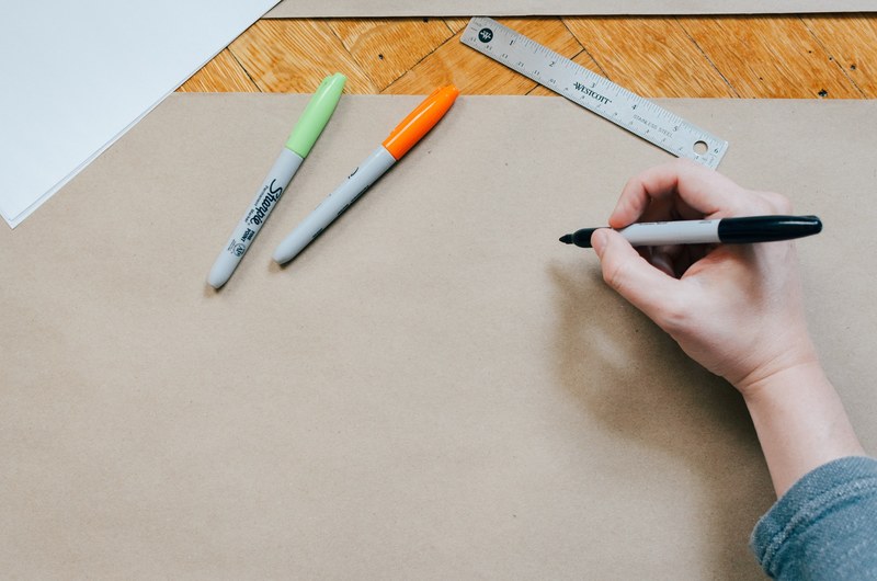 an overhead shot of a persons hand drawing on brown paper with a sharpie, design work 4k