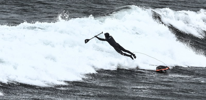 a man in a wetsuit holding a paddle jumping or falling off a paddleboard as a wave hits at wells, paddleboarder loses balance 4k
