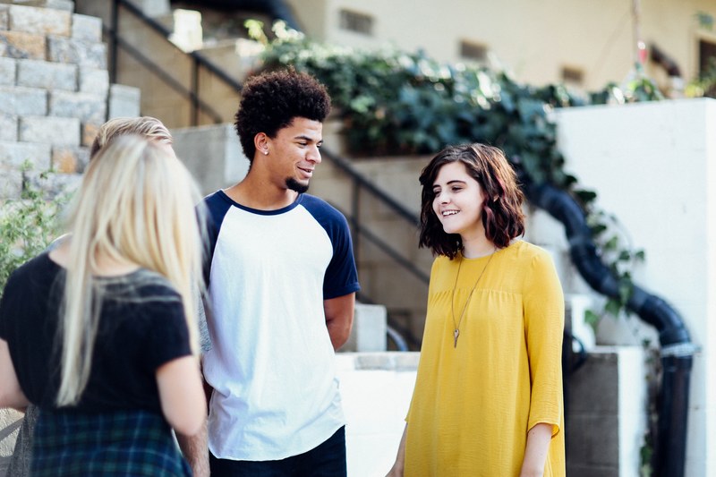 four young people smiling while talking near a staircase outside a building, young people in conversation 4k