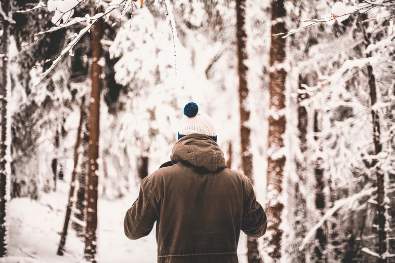 man with thick jacket and knit hat walking into white snowy forest, winter hike 4k