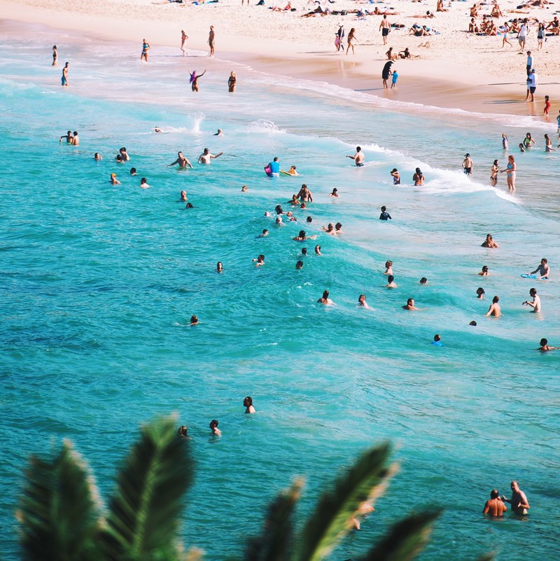 people splashing and swimming in azure sea near a sandy beach on a sunny day, beach life 4k