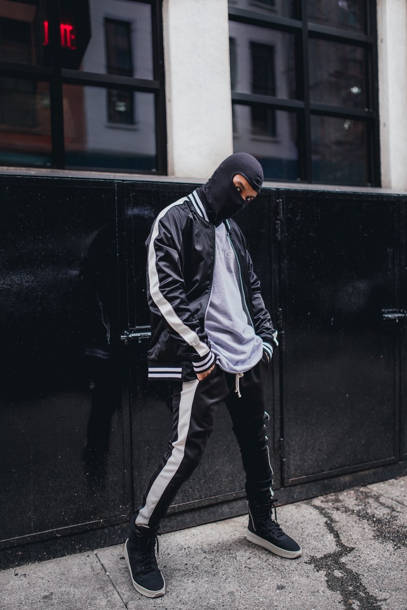 a man wearing a mask in a black tracksuit poses in front of a black and white building, man in a black mask 4k