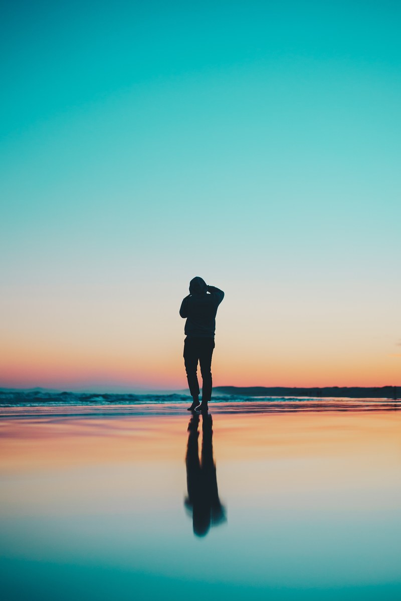 a man standing on the water at stockton beach with the sunset in the background, reflection of a silhouette 4k