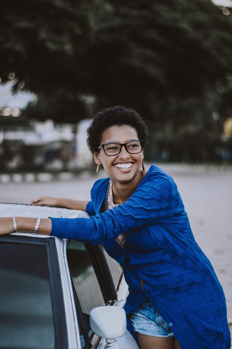 a smiling woman in glasses leaning against a car, smile 4k