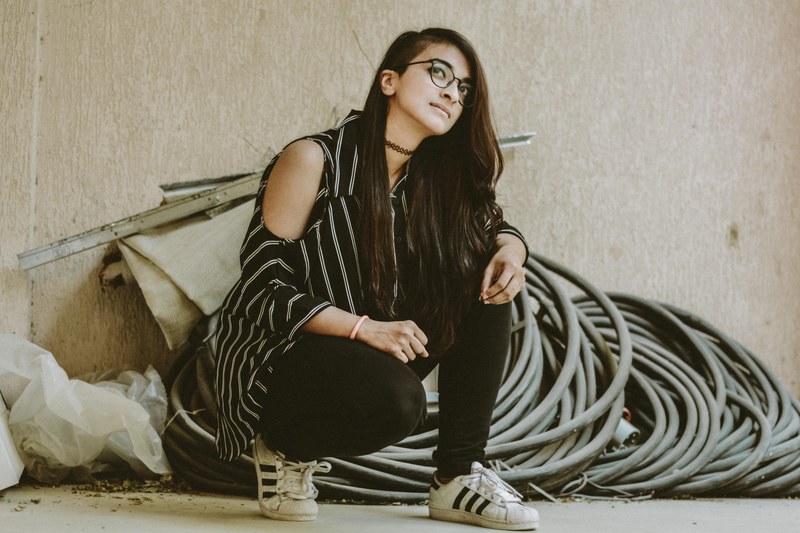 a woman with glasses in adidas kneels looking upward by piping and building materials, woman with piping 4k