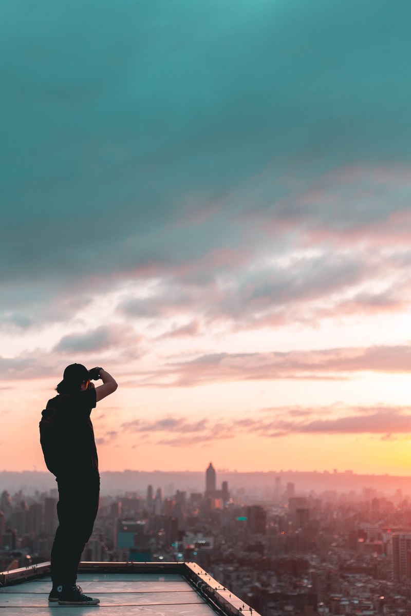 a photographer standing on a roof taking a photo of the taipei skyline at sunset, capture amazing scenery_ 4k