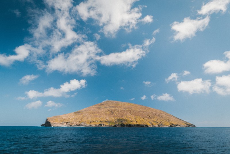 a small brown grassy island in the middle of the blue ocean with a bright blue sky, the island 4k