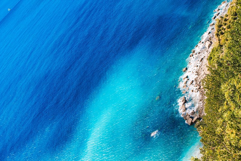 a drone shot of the deep blue sea and a rocky beach in cinque terre, paradise coast 4k