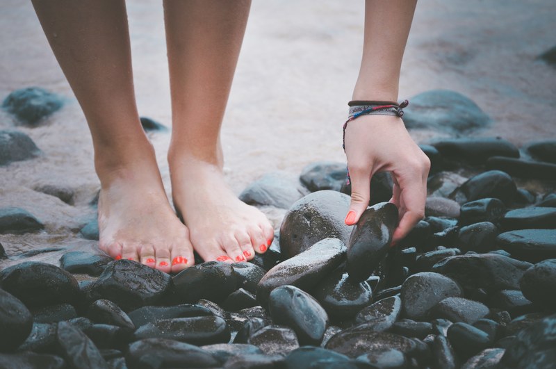 a low shot of a woman standing on wet pebbles and picking up one of them, picking up pebbles 4k