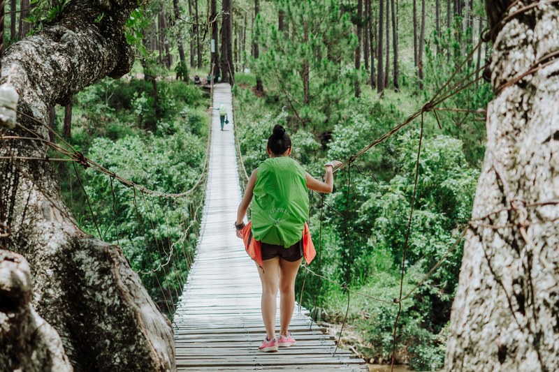 a person in a green pack walks down a suspended wooden footbridge in dalat, when in dalat 4k