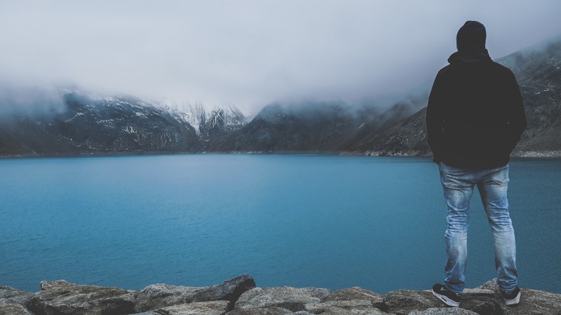 man looks out over calm waters at foggy snowy mountains, day 20 unsplashdaily 4k