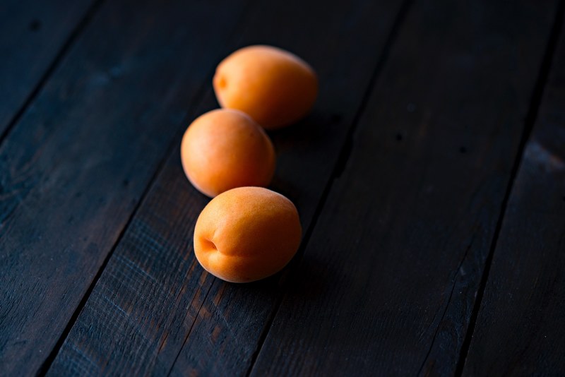 three apricots lined up on a wooden table, appricots 4k