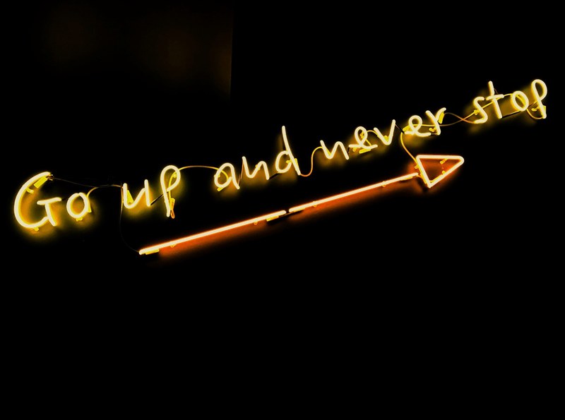 a yellow go up and never stop neon with a long arrow against a black background, never stop 4k