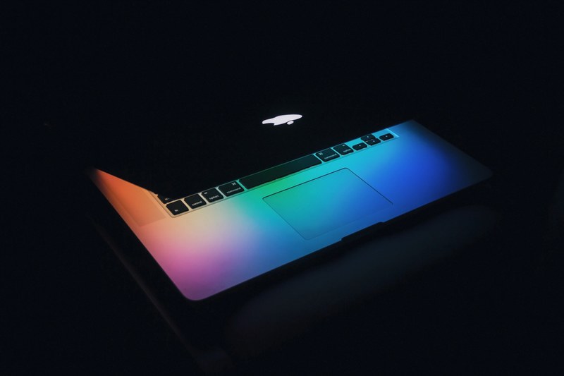 the screen of a half closed macbook illuminating the keyboard with various colors, colorful macbook keyboard 4k