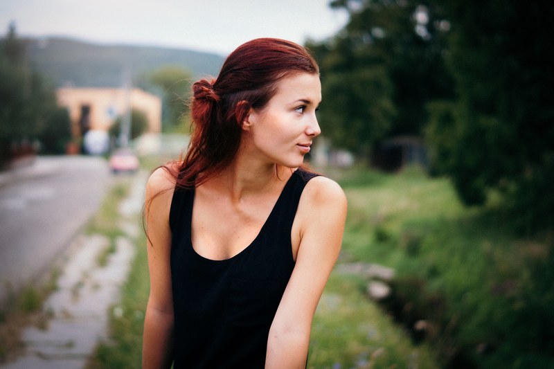 a woman in a black tank top looks over her shoulder against a blurry outdoor background, woman looks over her shoulder 4k
