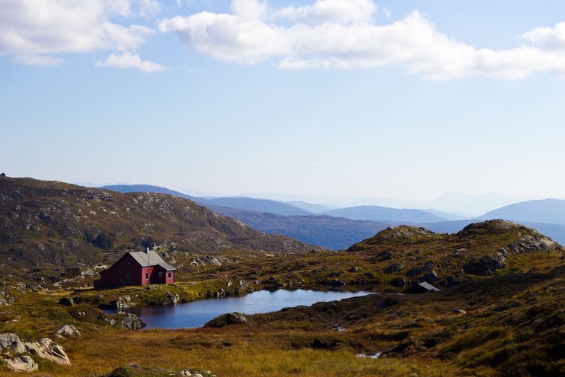 a red cabin near a small pond surrounded by rocky hills, red cabin on the fjords 4k
