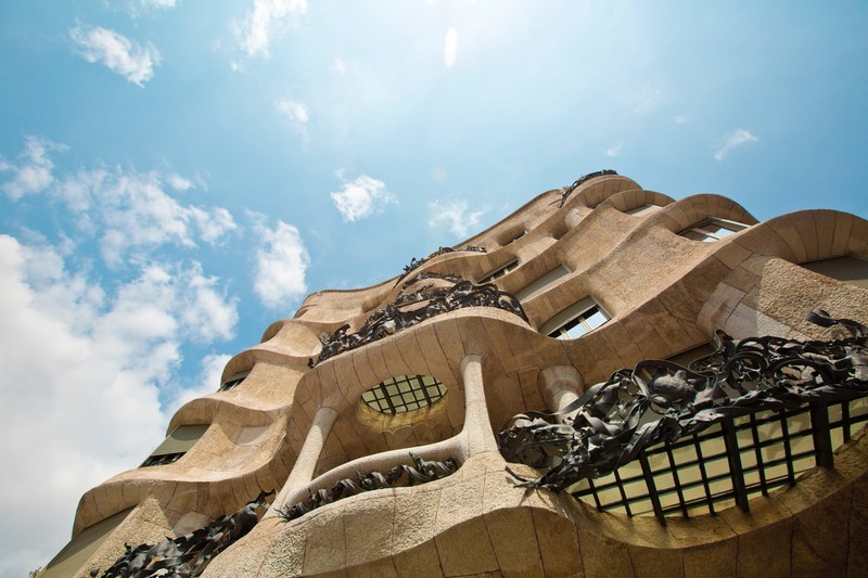 the facade of a building with sandstone architecture and blue sky with clouds in the background, staring up at a sandstone house 4k
