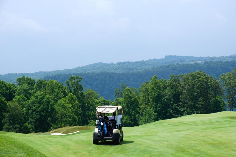 golf cart drives on highland course grass in front of green trees and hills, golf cart on grass 4k