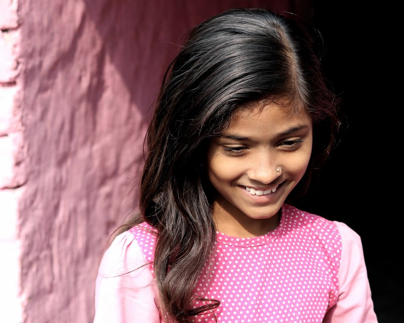 a smiling young girl in a pink shirt against a pink brick wall in kolkata, smiling girl in pink shirt 4k