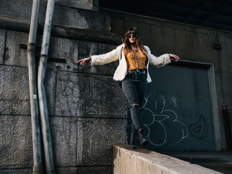 a woman wearing ripped jeans combat boots and a fur jacket walking on a wall in chinatown, woman posing by drainpipe 4k