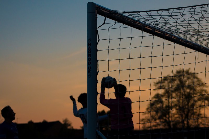three children play soccer at sunset at ewen fields, silhouette goalkeeper catching the ball 4k