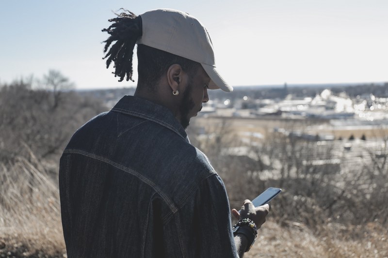 man with dreadlocks pulled through a baseball hat checking his phone, texting from a hilltop 4k
