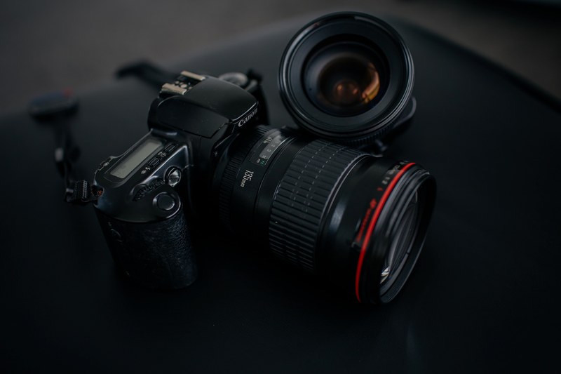 canon camera with 135mm lens and a strap beside another lens on a black surface, canon camera 135mm lens 4k