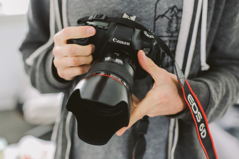 a close up of a photographer in gray sweater holding a canon eos 6d camera, _canon eos 6d camera 4k