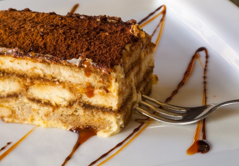 a slice of tiramisu drizzled with caramel besides a steel fork, traditional rich tiramisu cake with cinnamon 4k