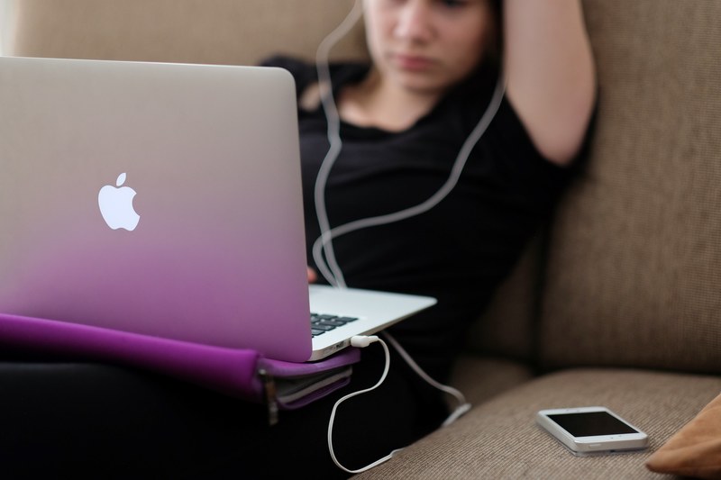 a woman using a macbook on a sofa with a white iphone nearby, woman with a macbook on a sofa 4k