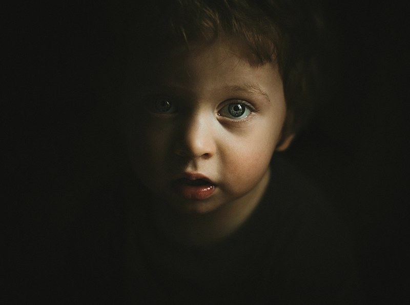 portrait of a young curious child with big eyes standing in the shadows, curious child 4k