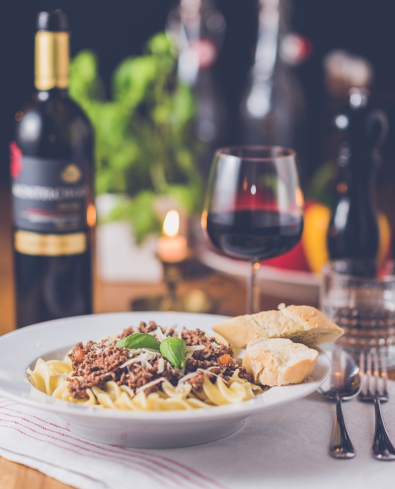 a plate with a pasta dish next to a wine bottle and a glass of red wine on a set table, romantic dinner for one 4k