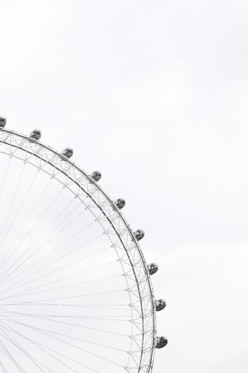 part of a ferris wheel with enclosed cars for riding in and people in the cars against an overcast sky, ferris wheel in a cloudy sky 4k