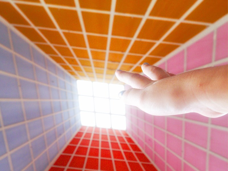 a hand reaching up to a sky lit window in a room surrounded by four different color walls with box patterns, _hand reaching top building 4k