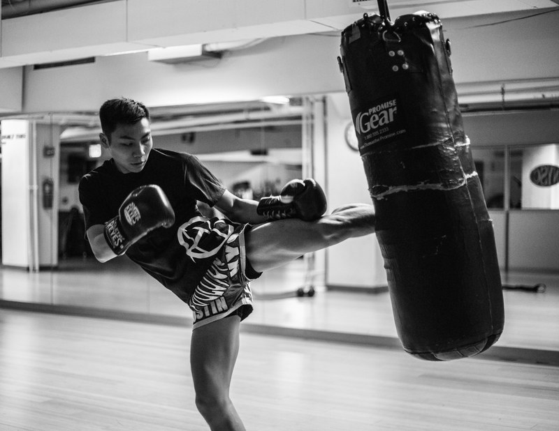 a man wearing boxing gloves kicking a punching bag at a gym in manhattan, bag work 4k