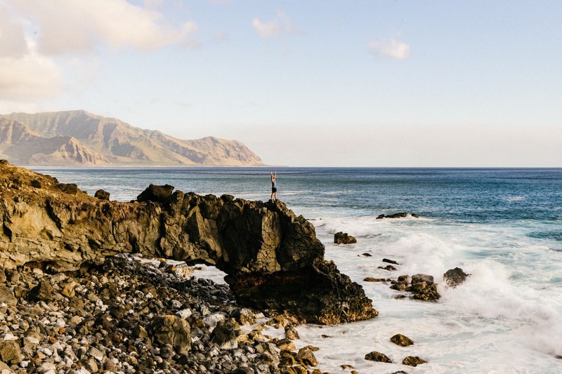 a person standing on the edge of a cliff by the sea with their arms outstretched, drinking in life 4k