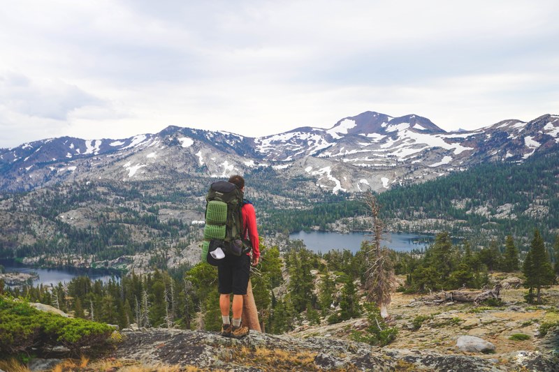 backpacker looks out at sparse forests and snowy mountains in desolation wilderness, desolation outlook 4k