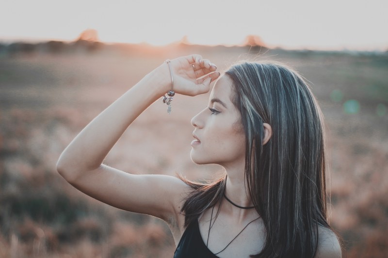 woman putting her hand to her head in a field at sunset, golden hour portrait 4k