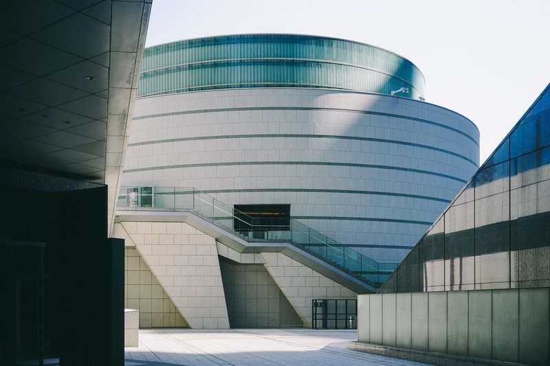 a stone and glass cylindrical building with stairs in the daylight, building in conrad tokyo 4k
