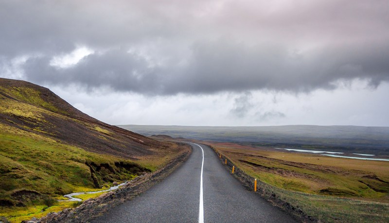 open road leads through a rural grassy hillside on a cloudy day, rural drive 4k