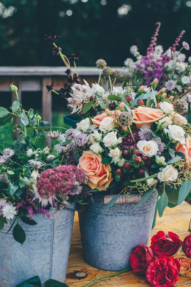 two colorful floral arrangements in tin pails with cut roses nearby, garden in a bucket 4k