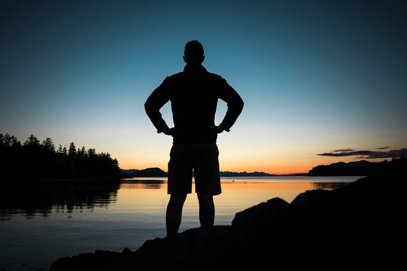 a silhouette of a man at the shore of a lake looking off into the distance at dusk, male silhouette over a lake 4k