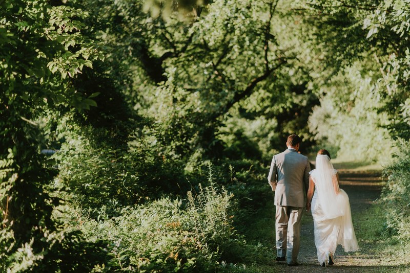 a bridal couple walking on a dirt path lined with trees, bride and groom walking in woods 4k