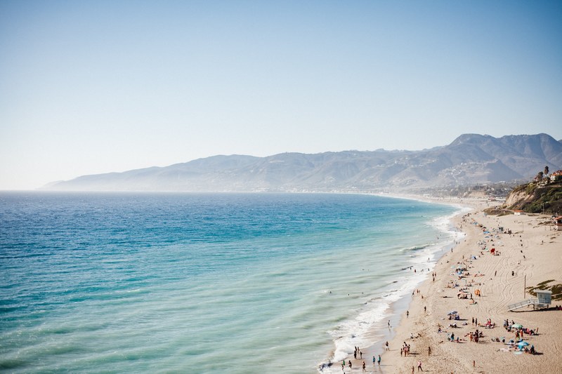 clean ocean washing up on sand shore filled with people in malibu, malibu ca 4k