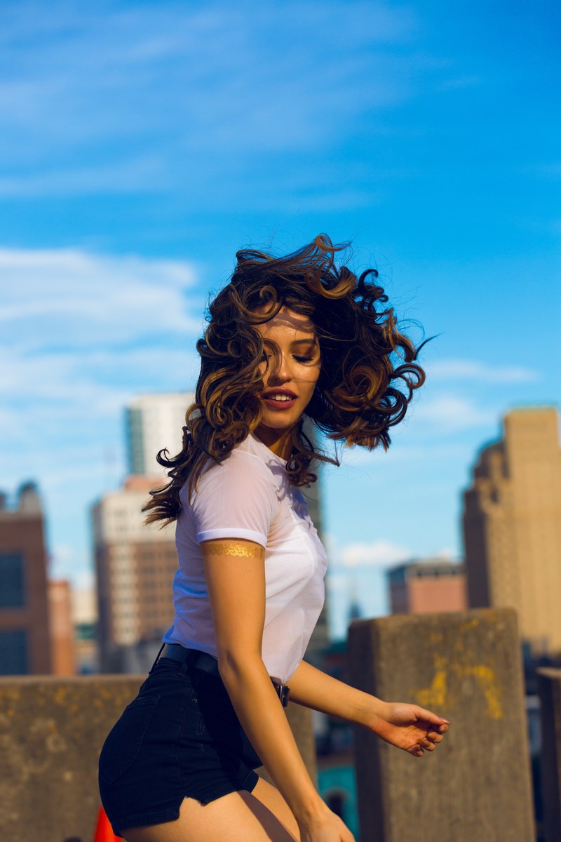 carefree woman with curly hair jumping in the air against a skyline, jumping for joy 4k