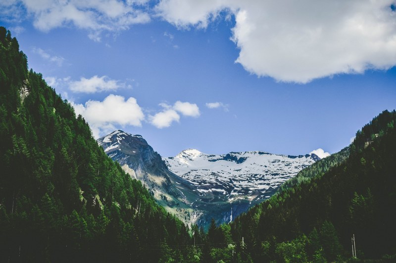 trees leading to icy mountains against cloudy blue sky, green wedge 4k