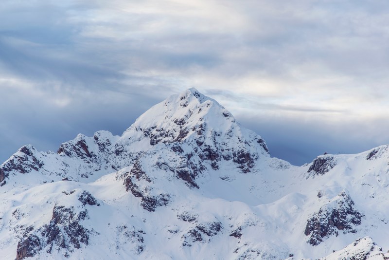 a rugged snow capped mountain summit against an overcast sky, alpine peak on a cloudy day 4k
