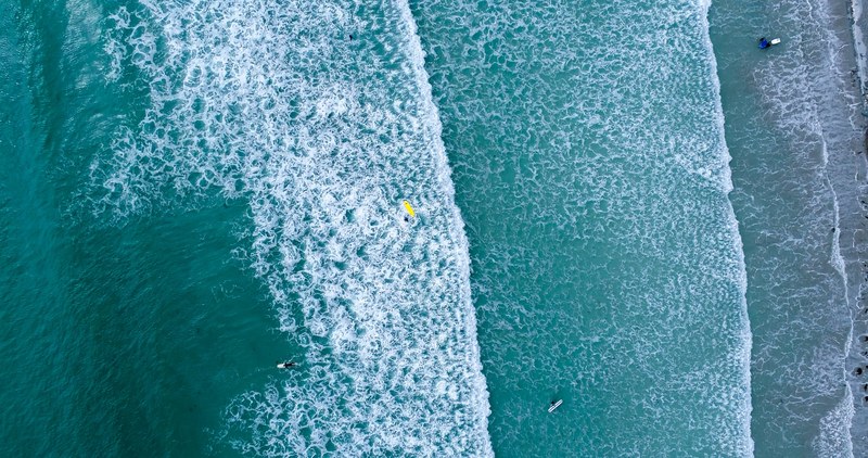 an overhead drone shot of surfers in the turquoise sea at vazon, surfing in vazon bay guernsey 4k