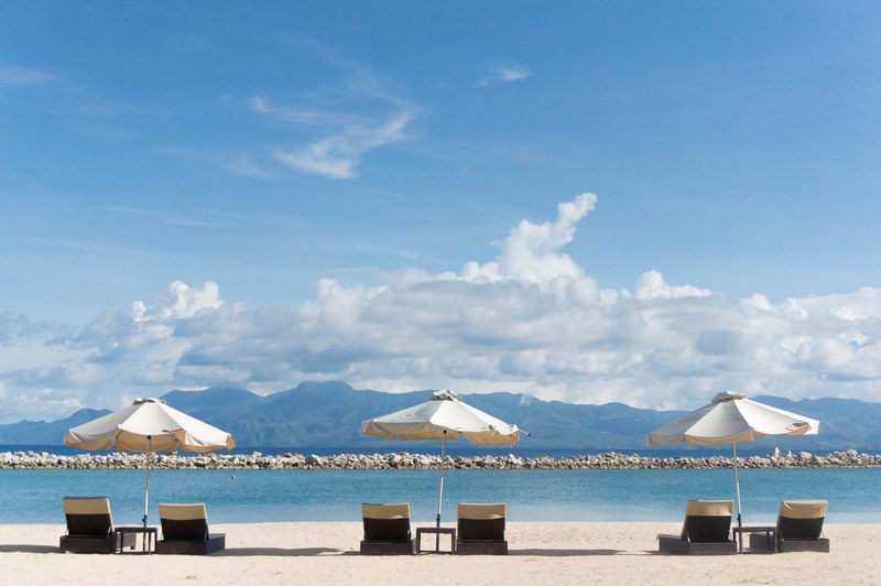 deck chairs under umbrellas on a sunny beach with view on tall hills, hilltops by the sea 4k